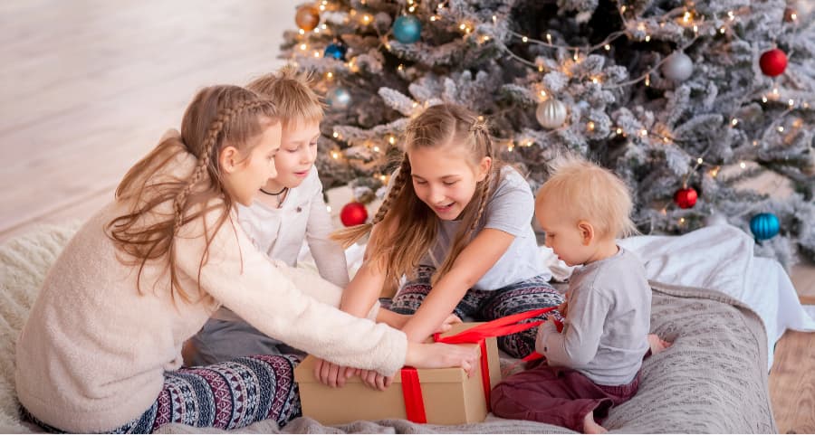 Kids opening a present in the living room beside a Christmas tree.
